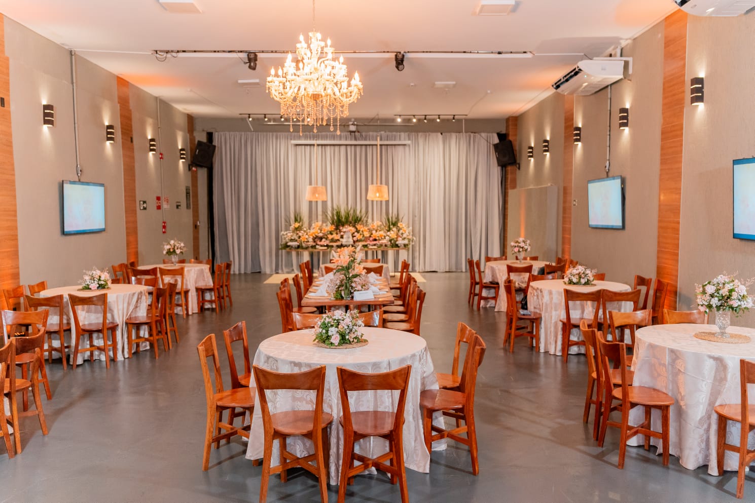 Salão principal do Jardins Caiçara com lustre de cristal, mesas redondas postas e arranjos florais